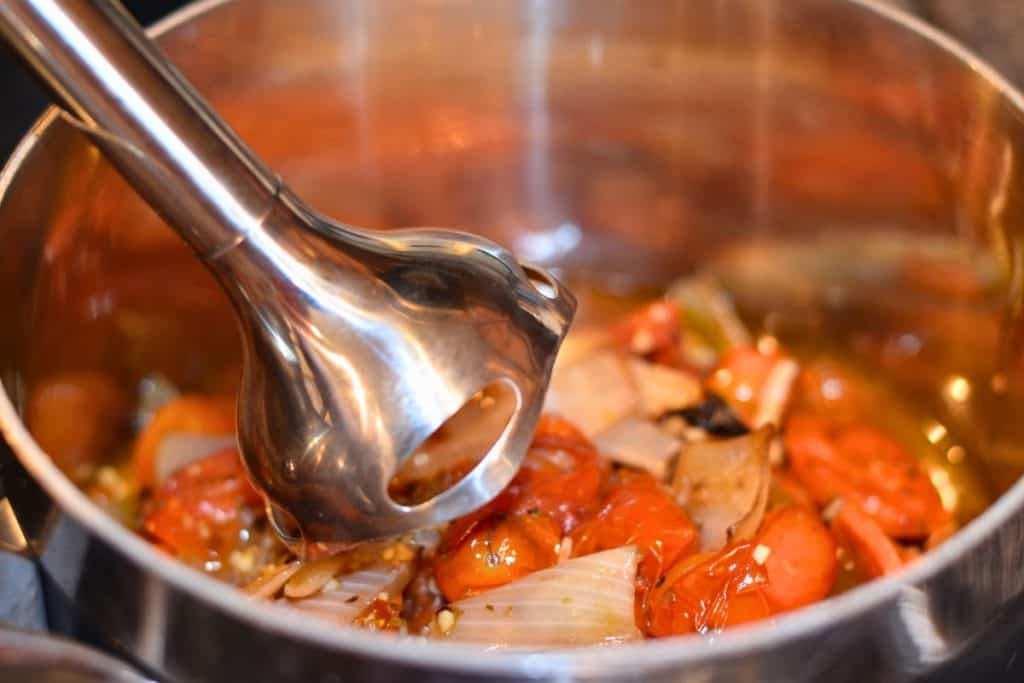 An immersion blender getting ready to blend the roasted vegetables.