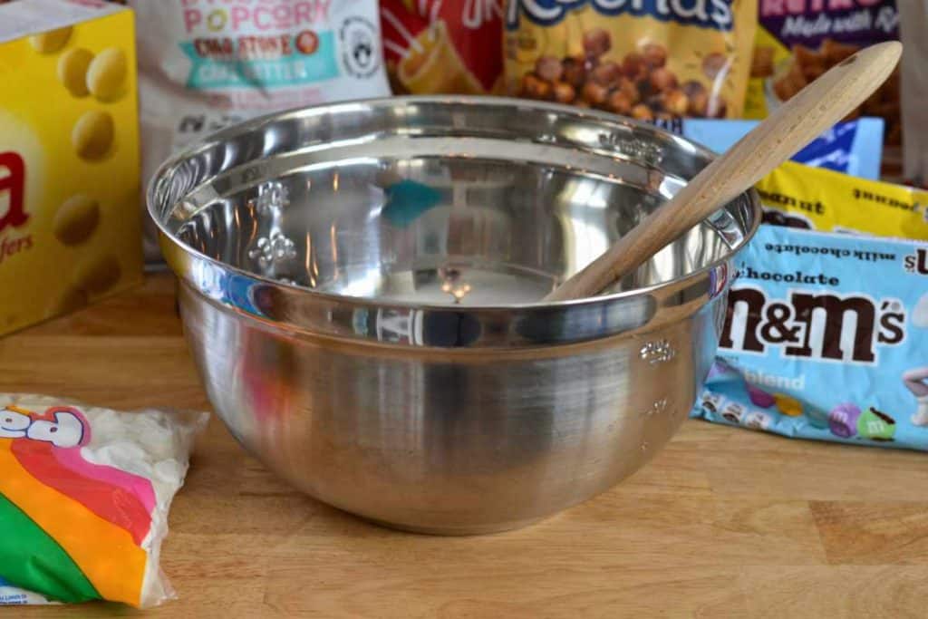 A stainless mixing bowl in front of all the ingredients for Easter Bunny Snack Mix