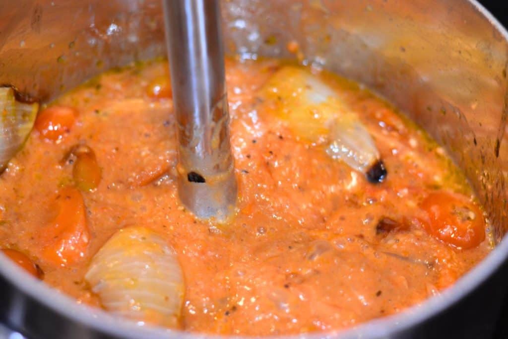 Halfway blended vegetables in a saucepan with an immersion blender in the pan blending the vegetables