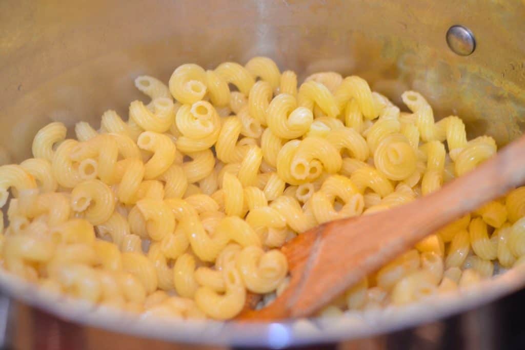 Cooked cavitappi pasta with a wooden spoon stirring it.