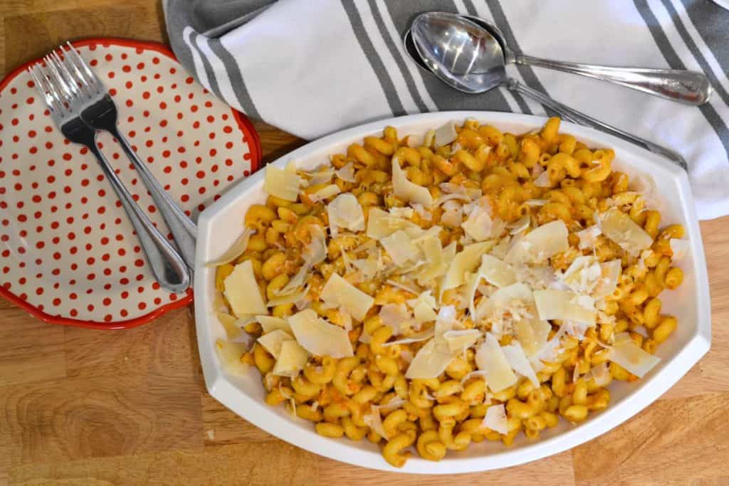 Roasted Cherry Tomato sauce with pasta on a serving platter with shaved parmesan cheese on top, looking at the dish from directly above. WIth napkins and plates and forks and spoons on the table with the pasta.