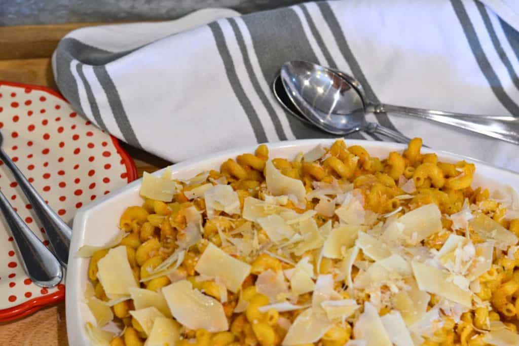 Close up of Roasted Cherry Tomato sauce with pasta on a serving platter with shaved parmesan cheese on top, looking at the dish from directly above. WIth napkins and plates and forks and spoons on the table with the pasta.