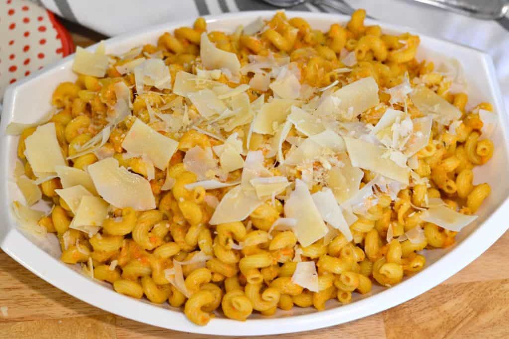 Close up shot of Roasted Cherry Tomato sauce with pasta on a serving platter with shaved parmesan cheese on top, looking at the dish from directly above. WIth napkins and plates and forks and spoons on the table with the pasta.