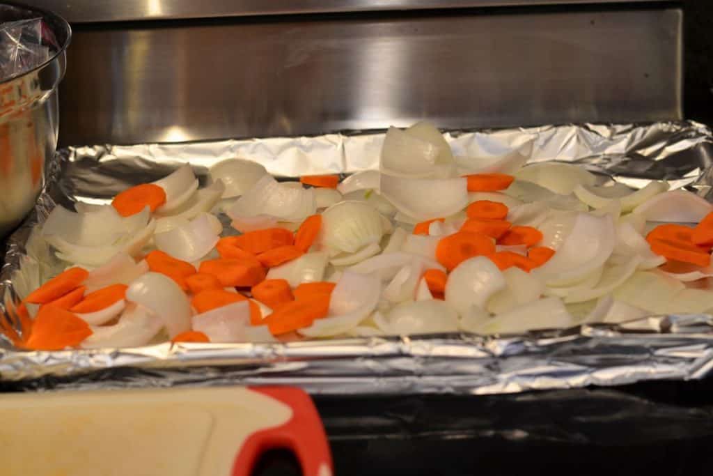 Sliced onions and sliced carrots on a foil lined baking sheet