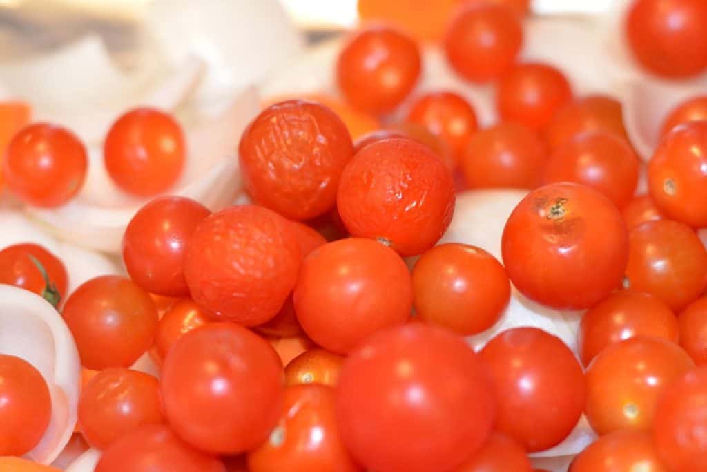 Cherry tomatoes on a baking sheet with onions close up showing flaws in some of the tomatoes