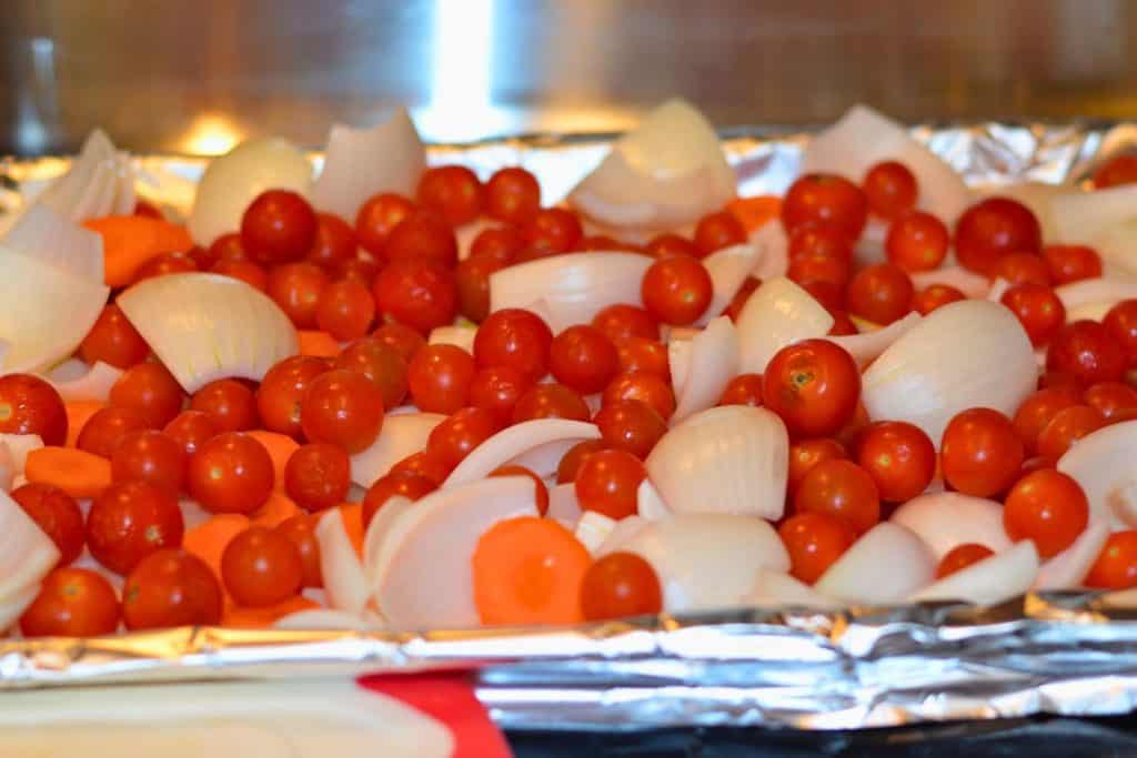 Cherry tomatoes, onions and carrots mixed together on a foil lined baking sheet