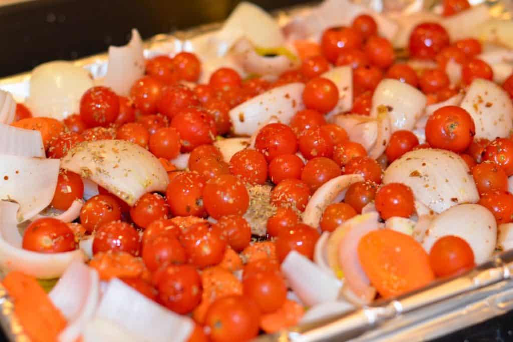 Italian seasoning and crushed red pepper sprinkled over tomatoes, carrots and celery on a foil lined baking sheet