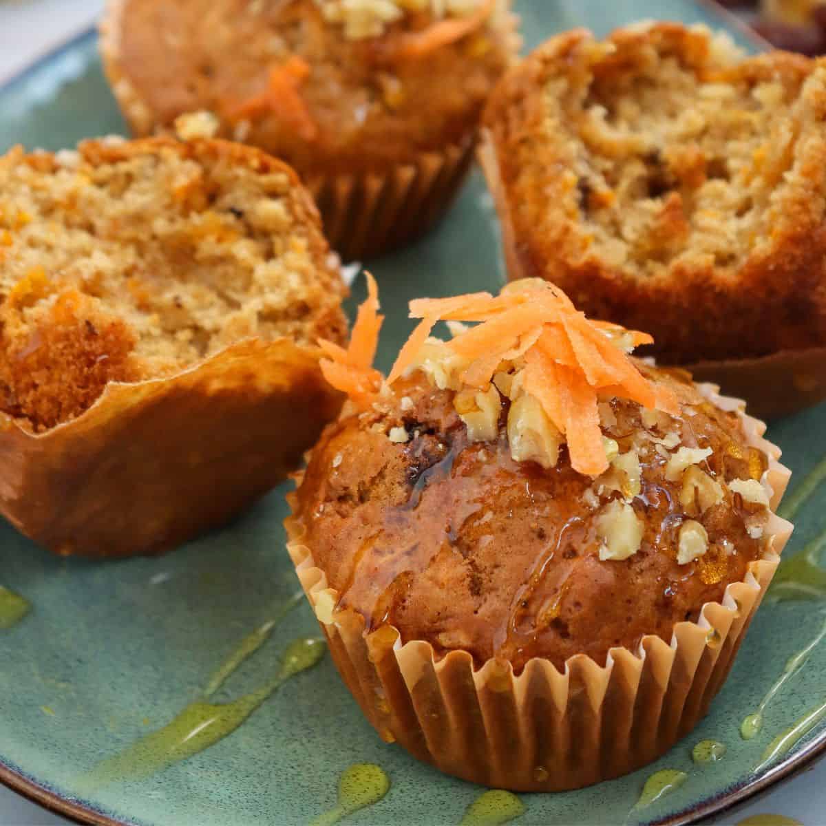 A close up of the carrot cake muffins drizzled in maple syrup and topped with a few shredded carrrots and walnuts