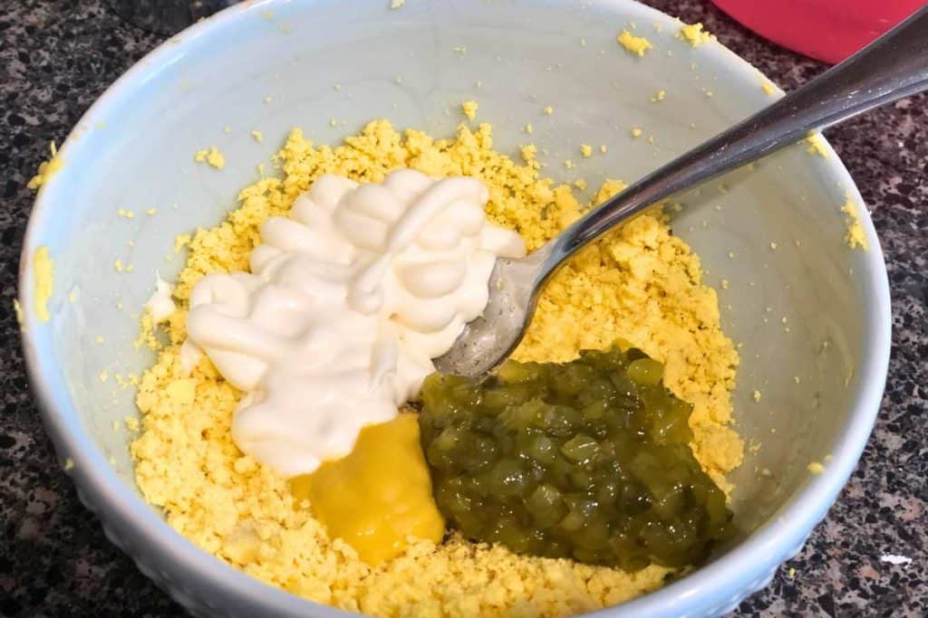 Deviled egg filling mixture before it's mixed together, including crumbled yolks, sweet pickle relish, mustard and mayonnaise.