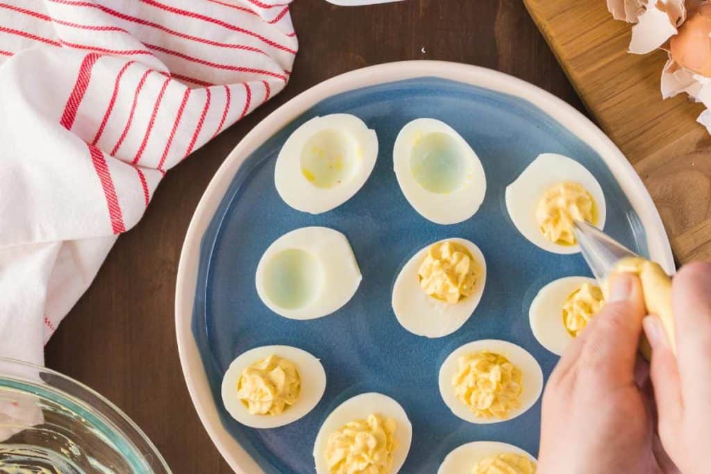 Plate with boiled egg halves with the filling being piped in to the egg white halves