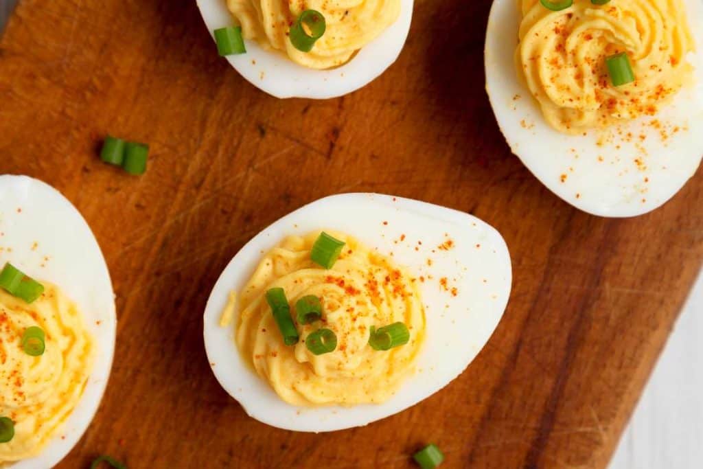 Deviled eggs on a wooden cutting board from above, with chives sprinkled on top of them