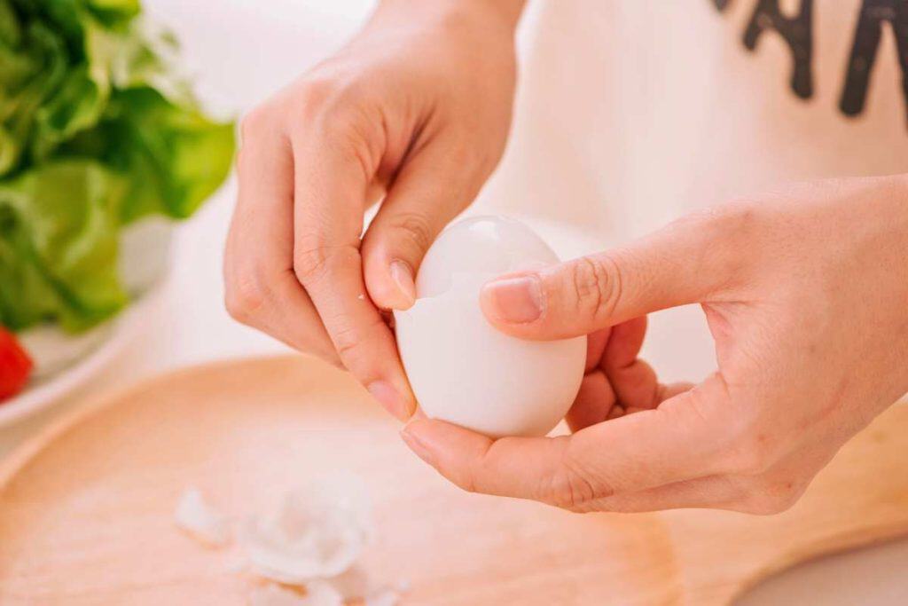 A woman's hands peeling a hard boiled egg