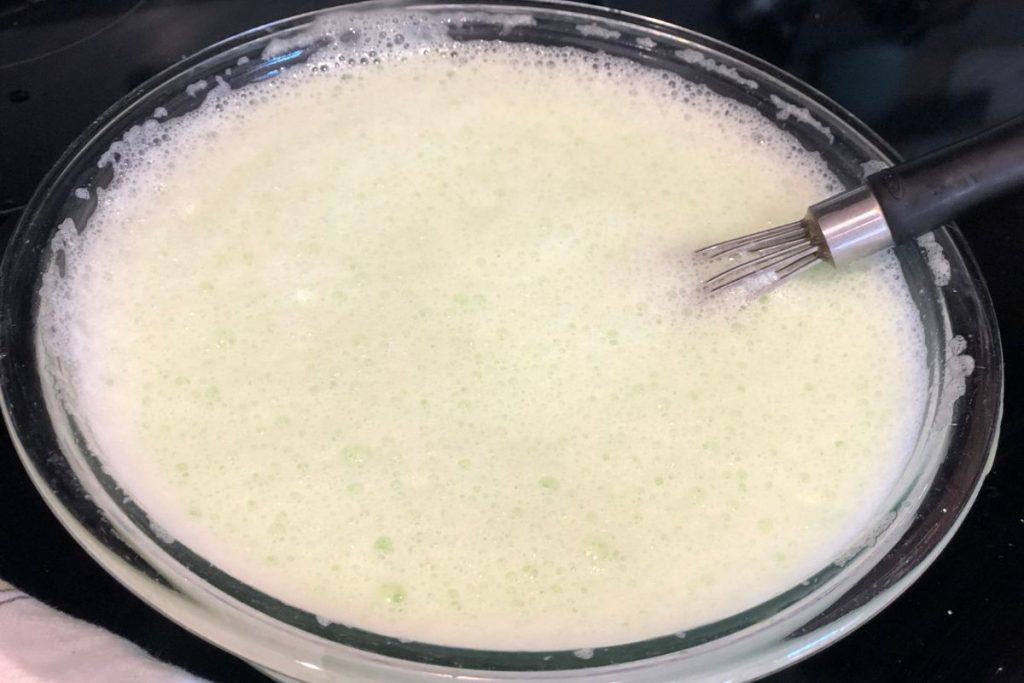 A glass mixing bowl with all the lime ice cream ingredients added and it is foamy as the Sprite carbonated drink has been added.