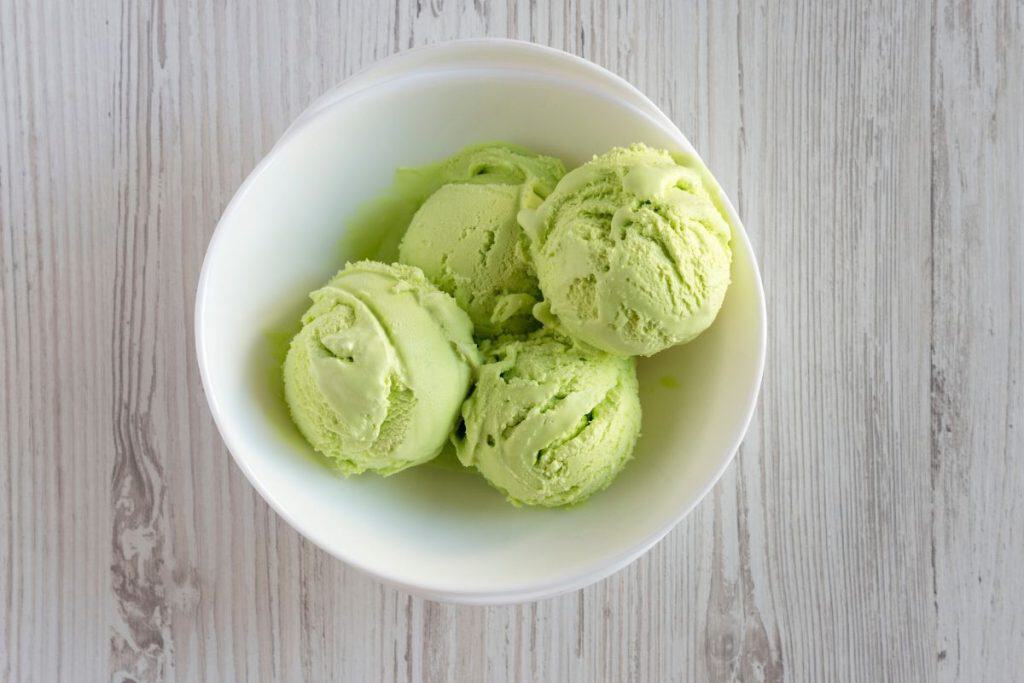 Four scoops of Lime kool-aid ice cream in a white bowl on a wooden table.