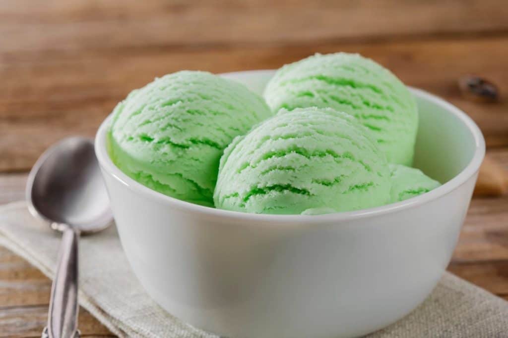 A white bowl filled with scoops of lime kool aid ice cream and aspoon and napkin on the side