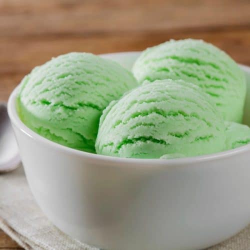 A white bowl filled with scoops of lime kool aid ice cream and aspoon and napkin on the side