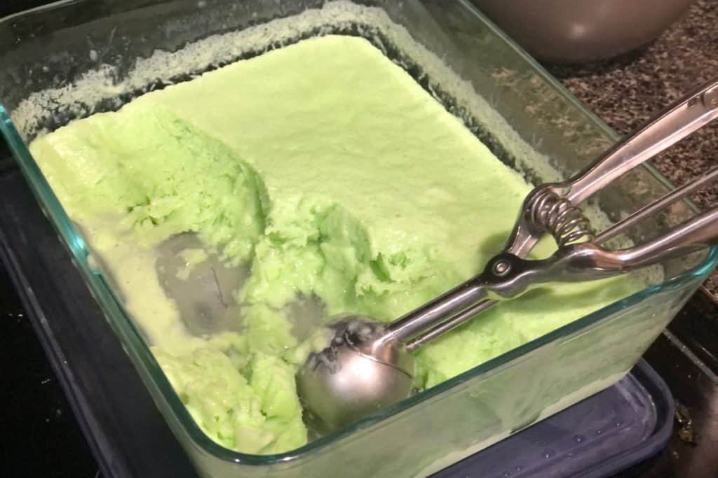 Scooping lime kool-aid ice cream from it's glass container that has been taken out of the freezer.