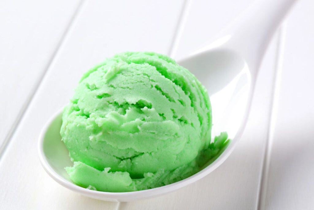 A scoop of Lime Kool-Aid ice cream on a white spoon on a table