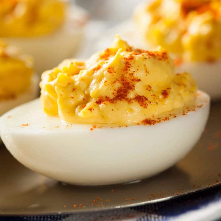 Close up of a deviled egg from the side with paprika sprinkled on top