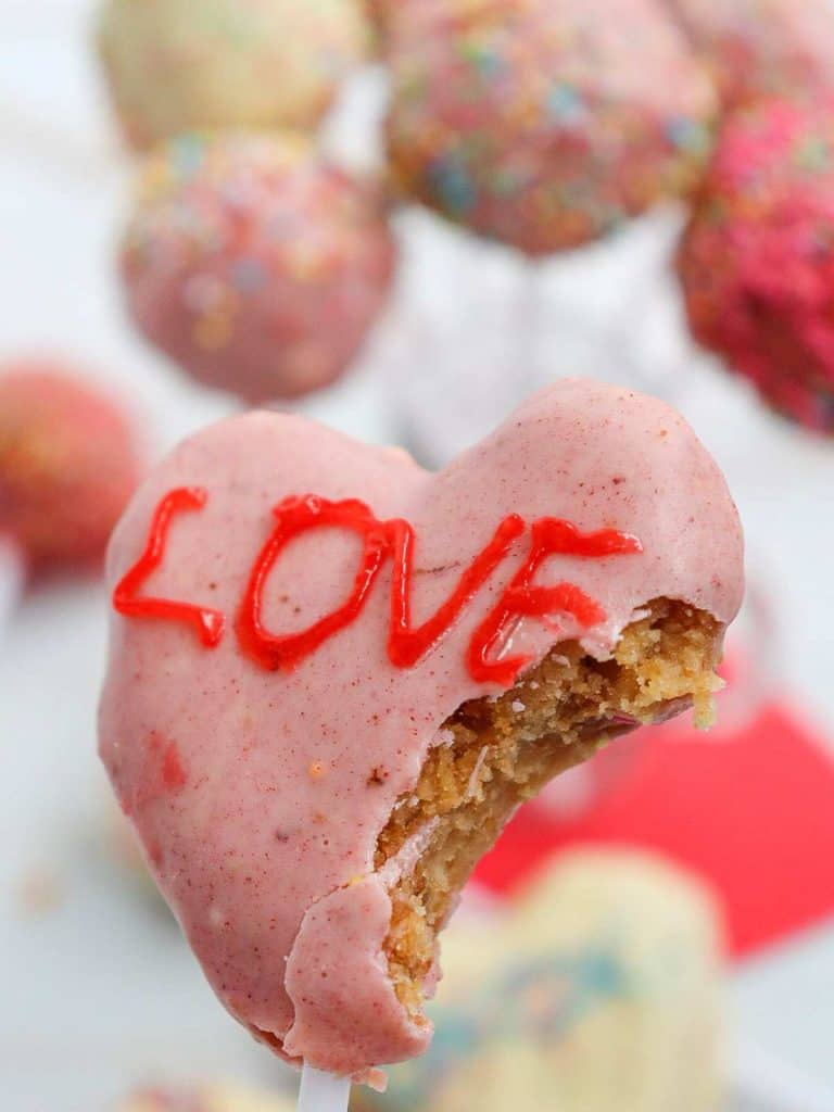A bite taken out of a heart-shaped cake pop that has the word "Love" written on it in icing.