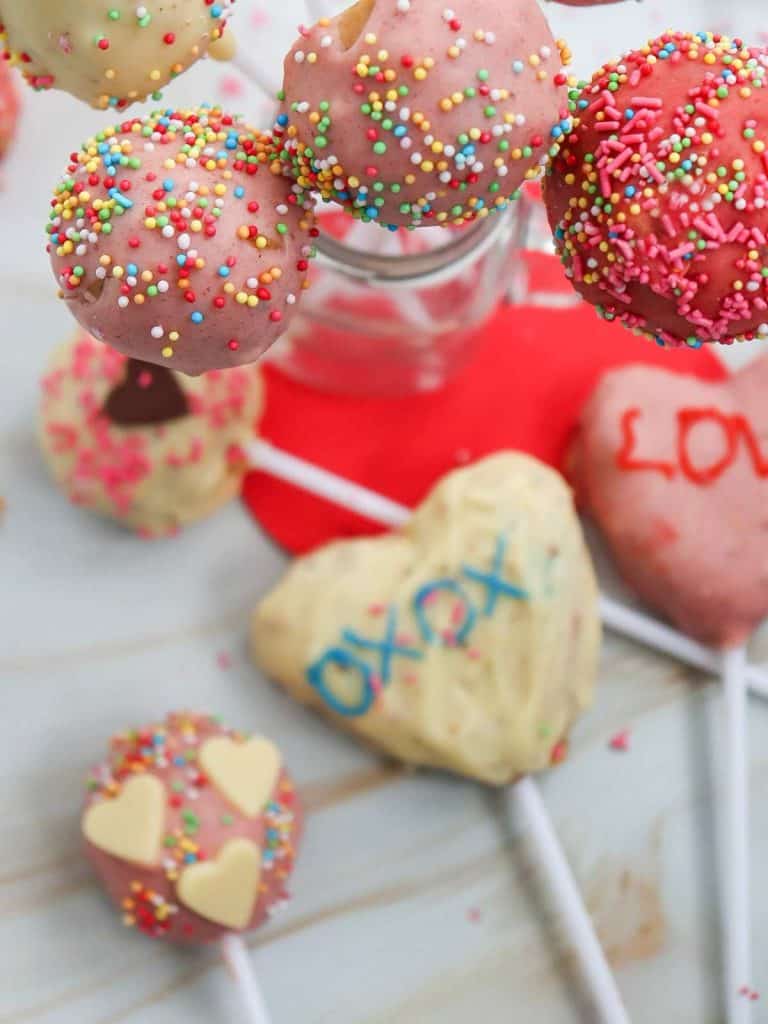 An upright shot of the cake pops in the jar and also lying on the table in the background of the picture.