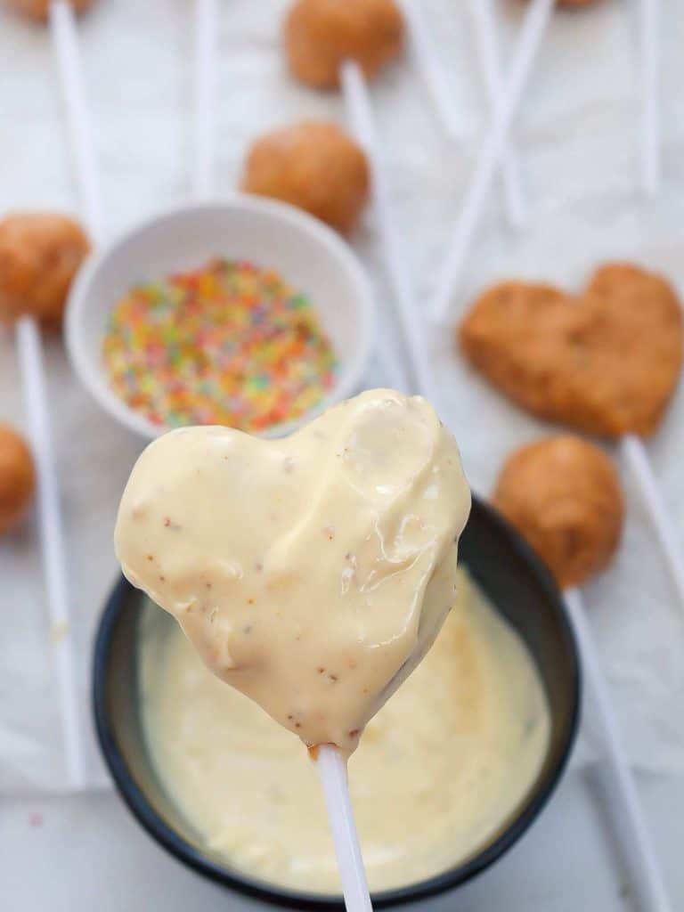 A heart-shaped cake pop that has just been completely submerged in the white chocolate and is now completely coated.