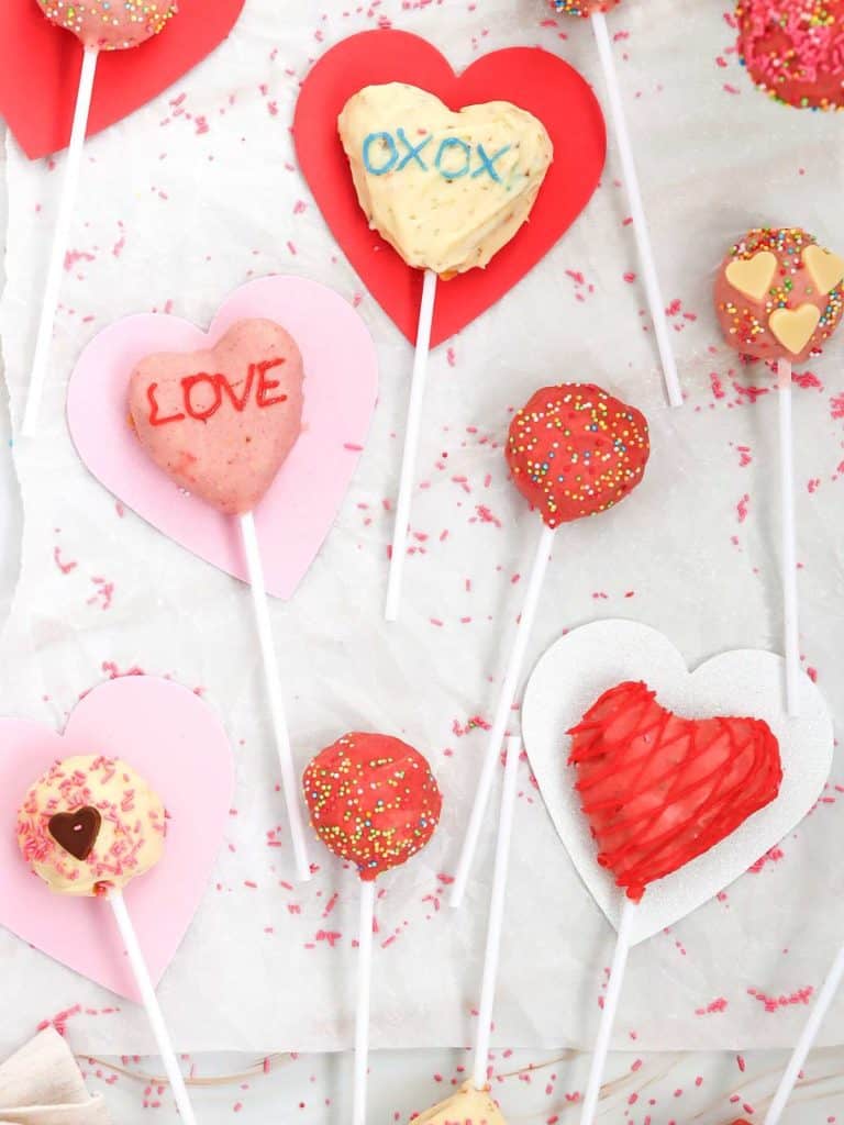 Some of the cake pops that were made into heart shapes lying flat on parchment paper with heart cut outs all around for decoration.