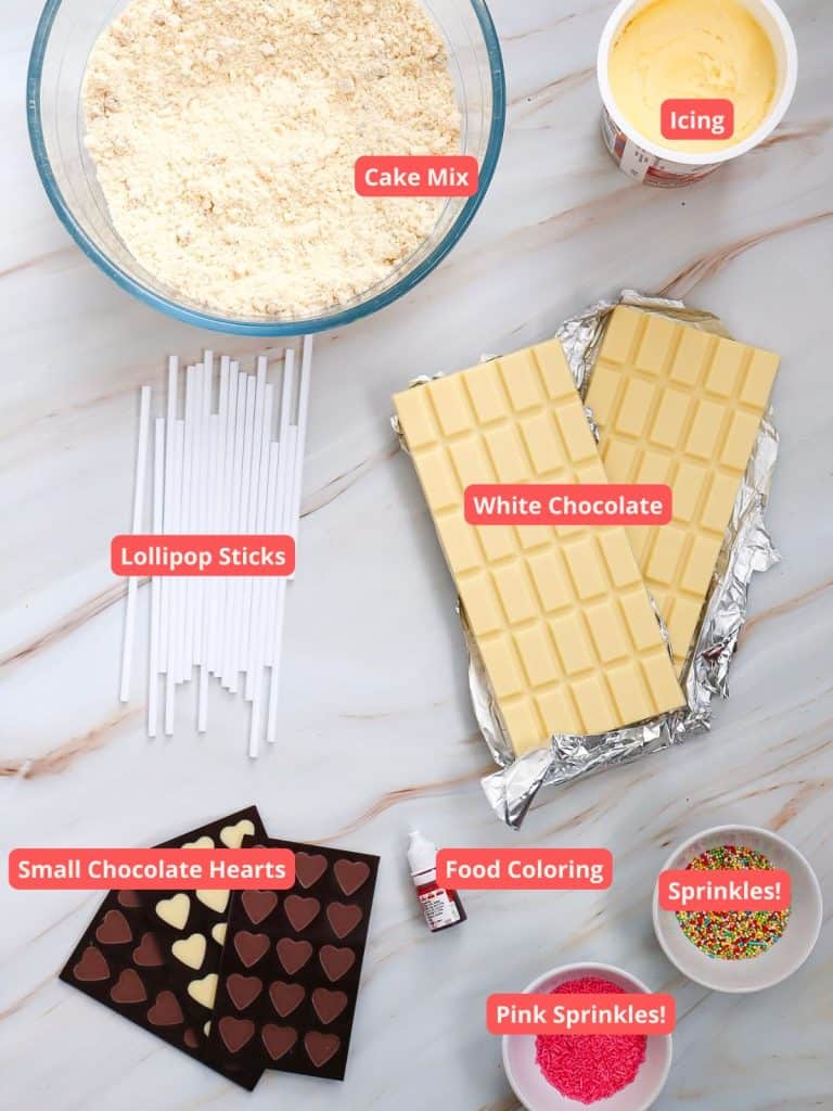 The labeled ingredients for the Valentine's Day Cake Pops, including cake mix, icing, white chocolate, lollipop sticks, chocolate hearts, food coloring and various sprinkles.