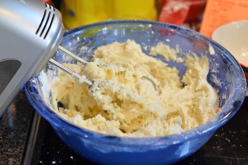 The first addition of flour added to a bowl of sugar cookie dough with an electric mixer.