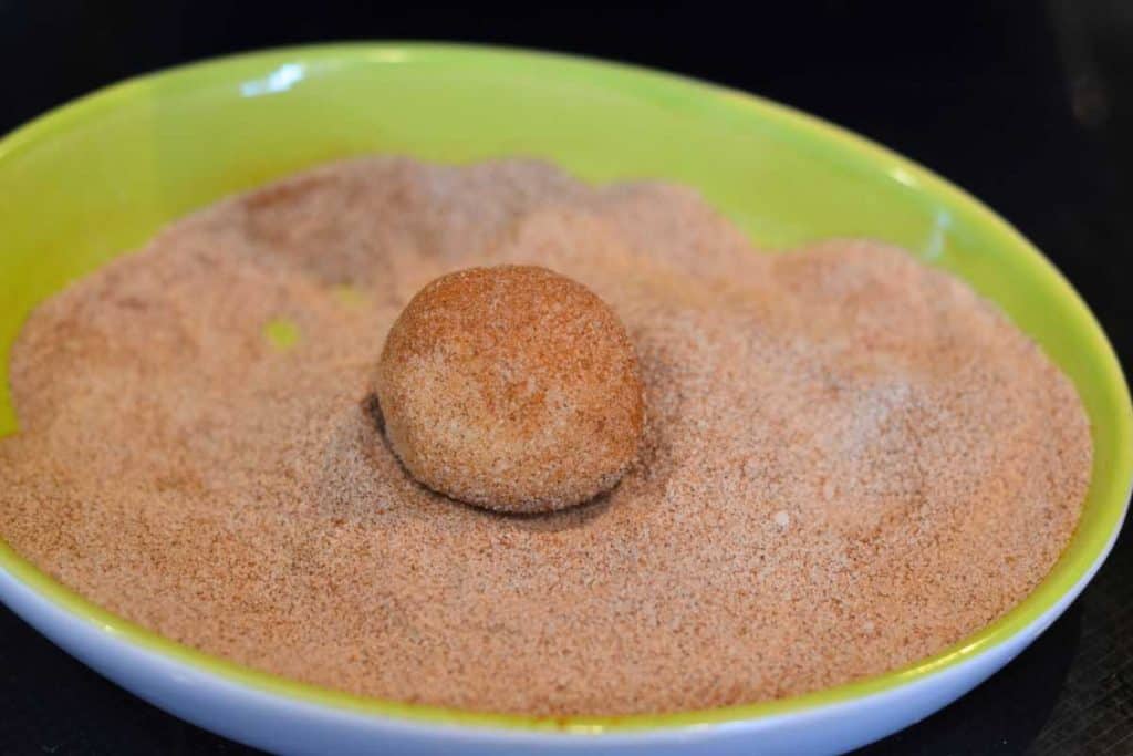 A ball of snickerdoodle cookie dough rolled and covered in cinnamon sugar.