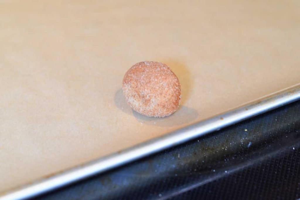A ball of prepped snickerdoodle dough on the baking sheet that's lined with parchment paper, ready to bake.