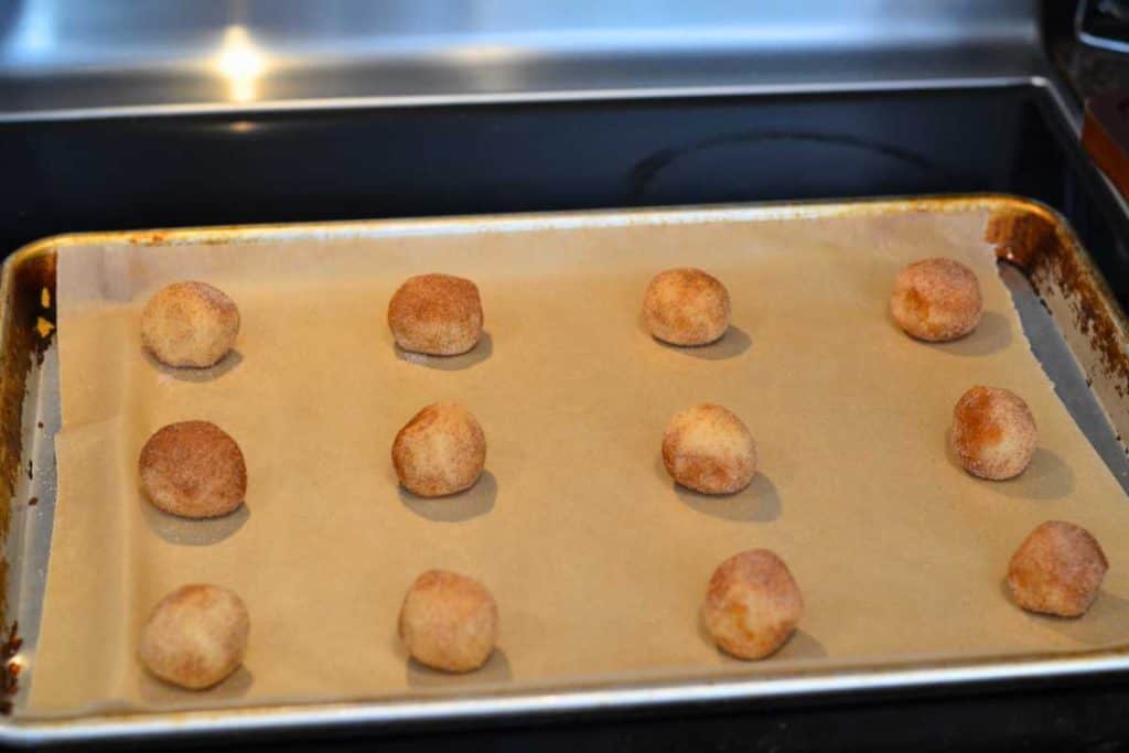 A baking sheet lined with parchment paper with snickerdoodle cookie dough balls ready to go into the oven