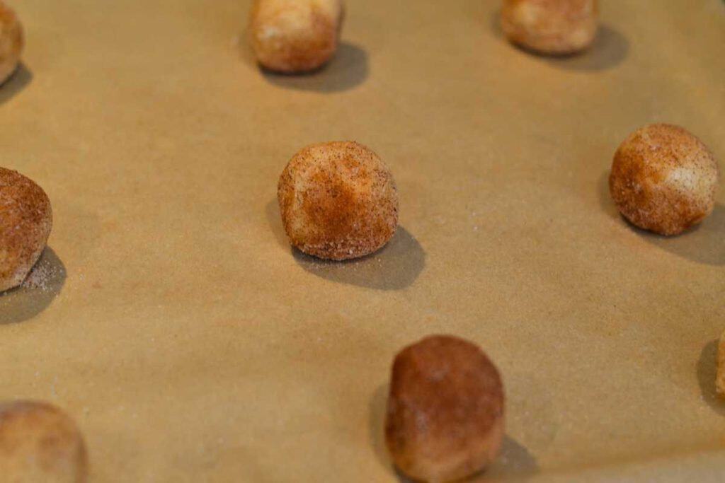 Snickerdoodle cookie balls close up on a baking sheet lined with parchment paper, ready to bake
