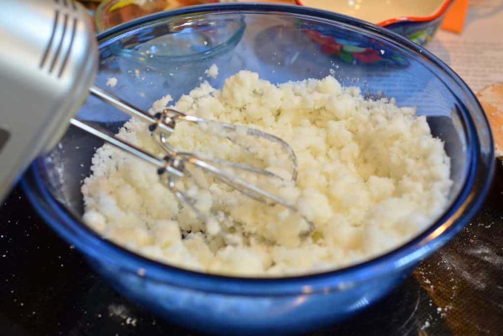 Sugar and shortening mixed together in a blue glass bowl with a hand mixer