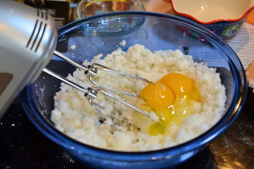 Two eggs added to the mixed sugar and shortening in a blue glass bowls with a hand mixer.