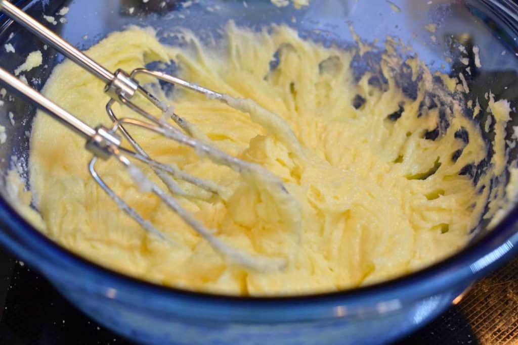 Snickerdoodle cookie dough mixed with all the ingredients except the flour in a blue glass bowl and an electric hand mixer.