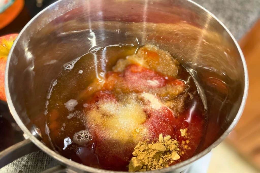 Dry spices added to the base of apple bbq sauce recipe in a saucepan.