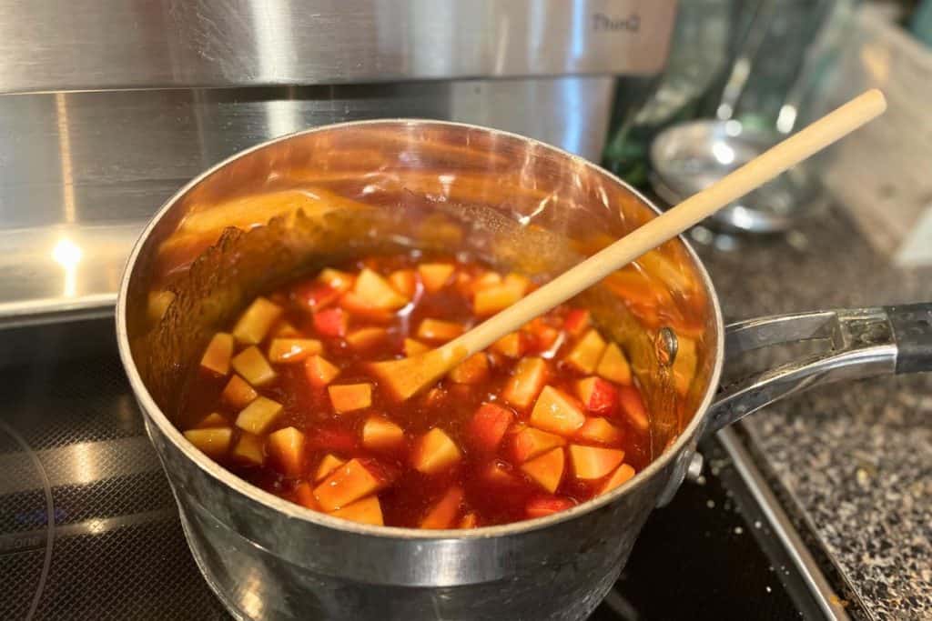 A saucepan on a stove with chopped apples in bbq sauce cooking.