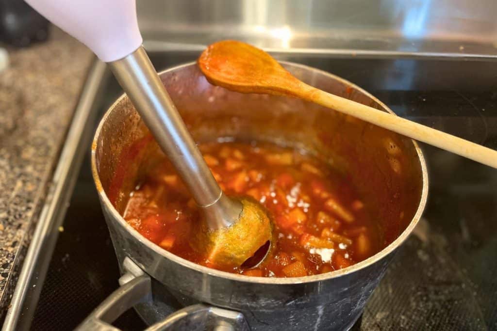 An immersion blender blending apple bbq sauce in a sauce pan