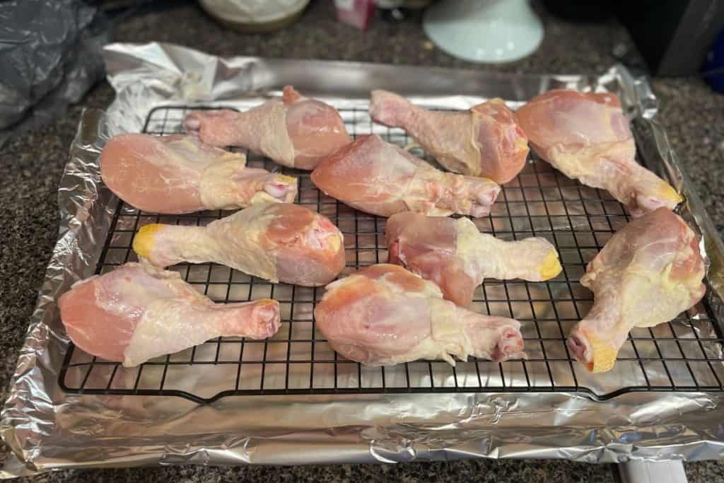 Raw chicken drumsticks on a baking rack on top of a lined baking sheet