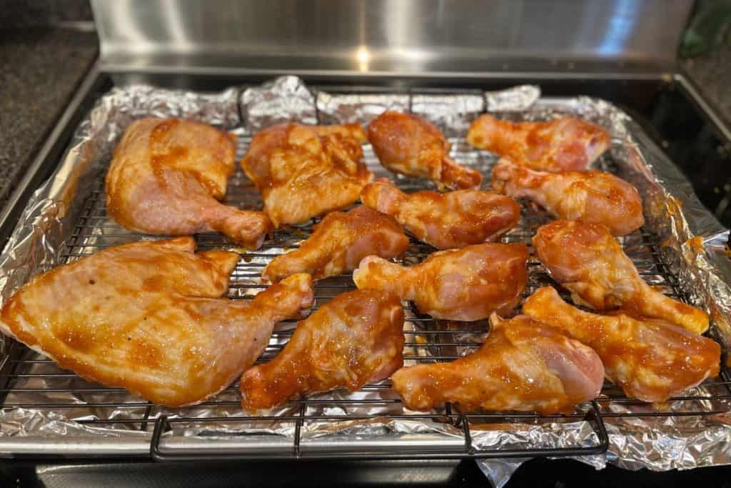 Raw chicken drumsticks on a baking rack on top of a lined baking sheet that have been brushed with bbq sauce before baking.