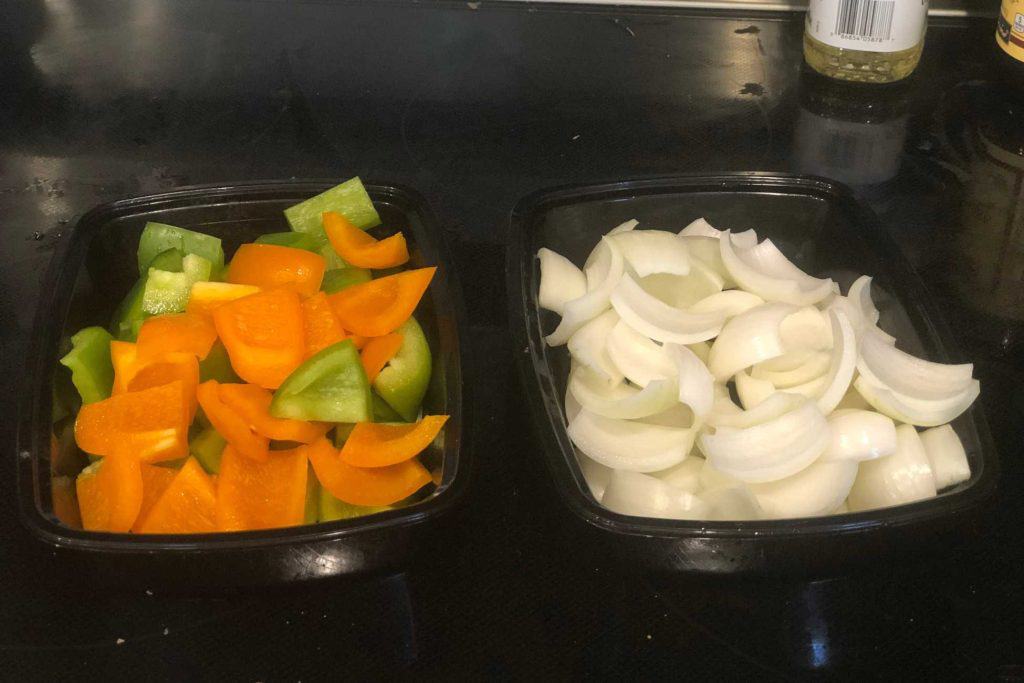 A container of sliced bell pepper and a container of sliced onions, ready to be put onto kebabs.