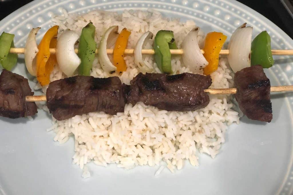 Finished beef and veggie kebabs on a plate with rice