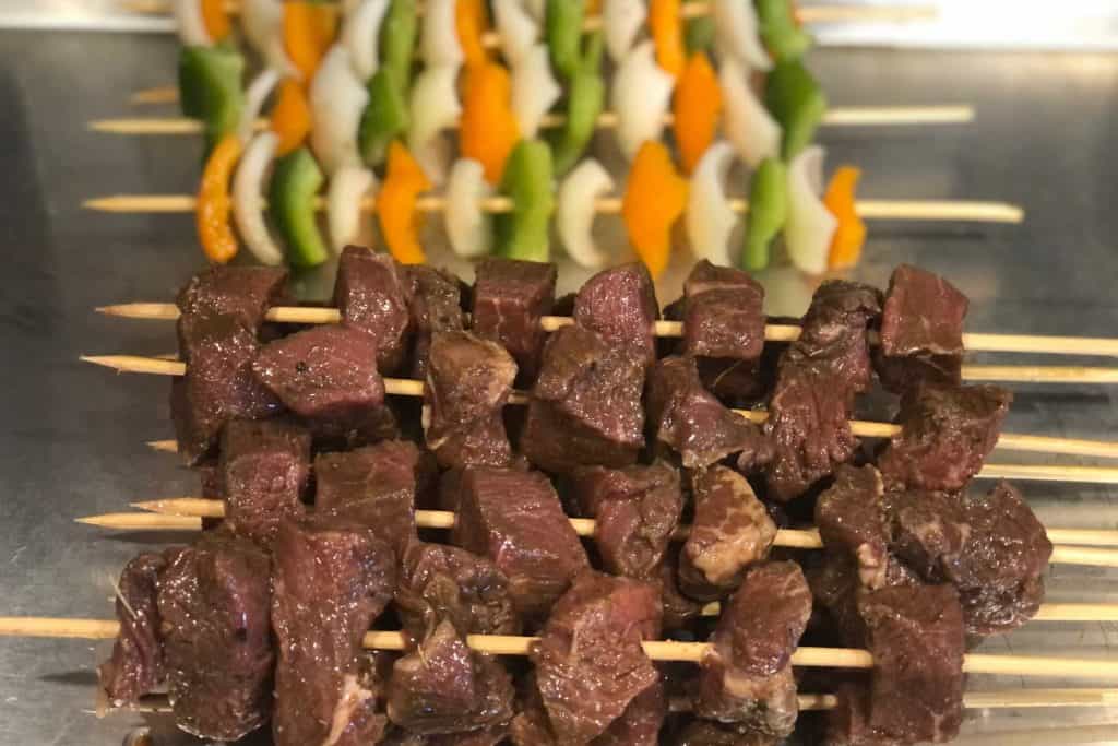 Marinated Mediterranean beef kebabs raw and on skewers ready to grill. Bell pepper and onion skewers are in the background