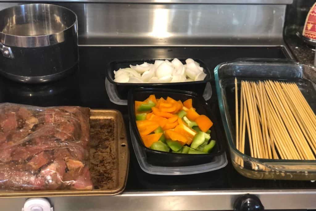 All the components to assemble kebabs, the marinated meat, the peppers, onions and soaked skewers