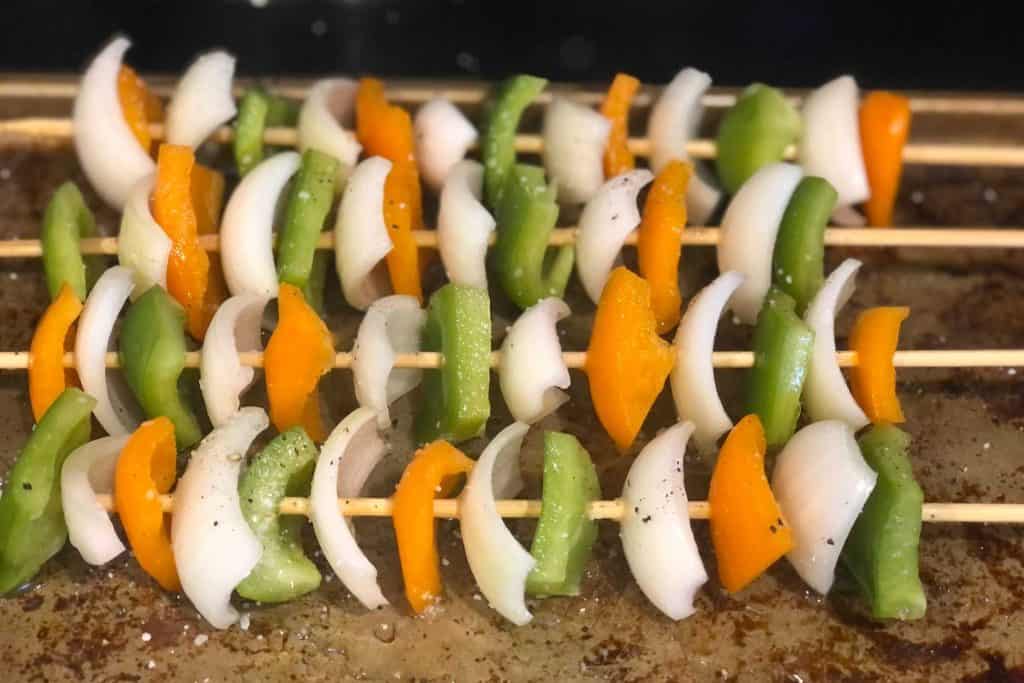 Onions, green bell peppers and a yellow bell pepper on wooden kebab skewers