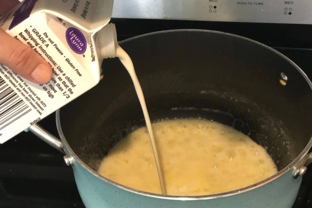 Pouring heavy whipping cream into a pot with butter, flour and onions cooking in the bottom of the pot.