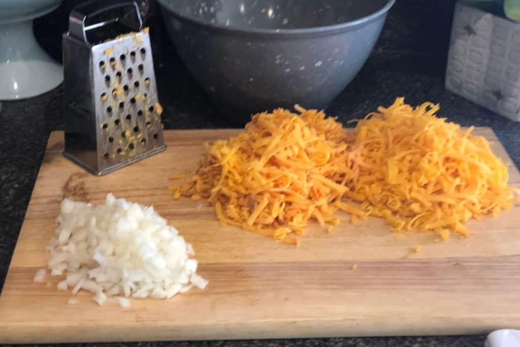 Shredded cheese and chopped up onion on a cutting board