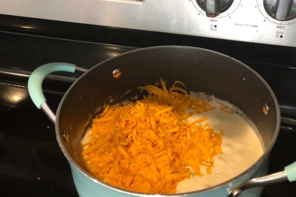 Adding cheddar cheese to the sauce as part of the instructions for Smoked Cheddar Macaroni and Cheese recipe