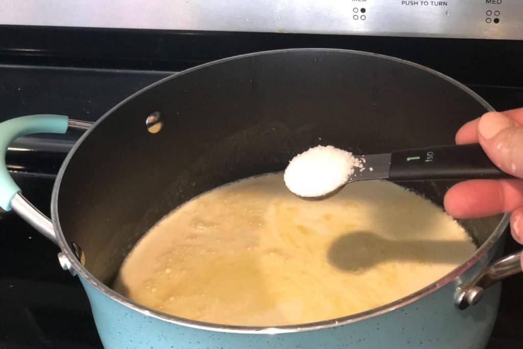 Adding salt to the recipe into the pot of the sauce for Smoked Cheddar Macaroni and Cheese recipe